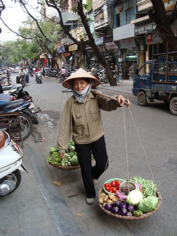 Prodavačka zeleniny v typickém kuželovitém klobouku s vahadly.
